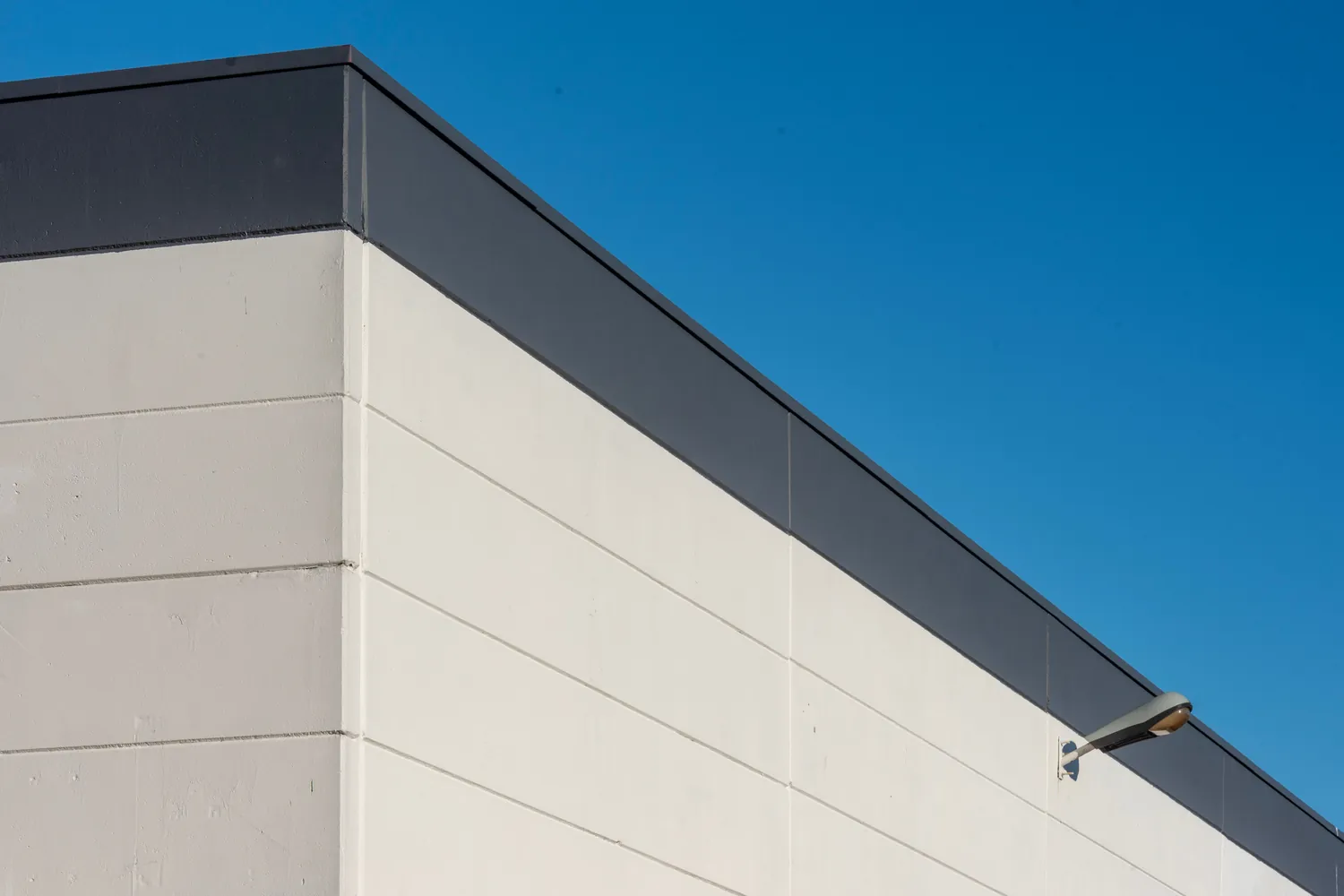 Gewerbehalle von aussen: Betonfassade und Attika eines Flachdachs vor blauem Himmel